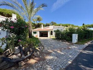 A house with a paved driveway leading to a covered entrance, surrounded by greenery and a clear sky. - VILAMOURA VINTAGE VILLA WITH POOL by HOMING (Vilamoura)