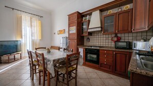 A kitchen with wooden cabinets, a dining table with chairs, a refrigerator, a stove, and a microwave. - CASA SAURO 10 (Avola)