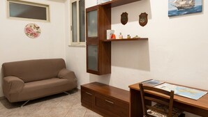 A room with a brown sofa, a wooden desk with a chair, a window, and wall decorations including a ship painting and a shield. - CASA SAURO 10 (Avola)