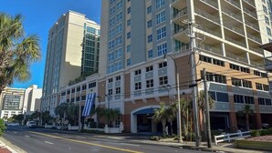 A multi-story hotel with a modern facade, a parking garage, and a street view with palm trees. - Ocean Drive. 3 bedroom 3 bath condo with an OCEAN VIEW (from side). Sleeps 10. (North Myrtle Beach)