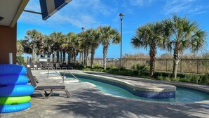 A swimming pool area with lounge chairs, palm trees, and a fence. - Ocean Drive. 3 bedroom 3 bath condo with an OCEAN VIEW (from side). Sleeps 10. (North Myrtle Beach)