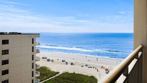 A beach view from a balcony overlooking a sandy beach with umbrellas and a lifeguard tower. - Ocean Drive. 3 bedroom 3 bath condo with an OCEAN VIEW (from side). Sleeps 10. (North Myrtle Beach)