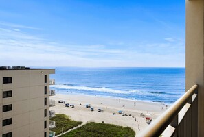 Blick auf einen Strand vom Balkon aus, mit Sonnenschirmen und einem Rettungsturm.