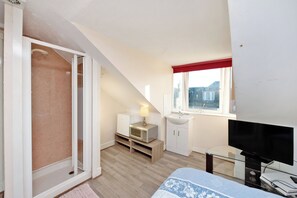 Un dormitorio con cama, televisión, microondas, lavabo y ventana con cortina roja.