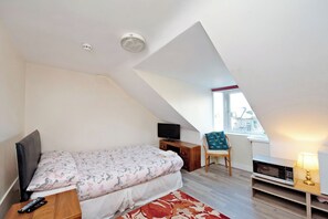 Un dormitorio con cama, televisor, silla, escritorio y ventana.
