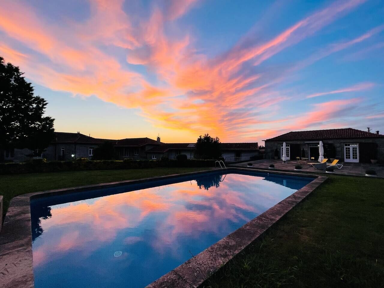 Una piscina con vista despejada del cielo durante el atardecer, rodeada por una zona residencial con casas y un patio.