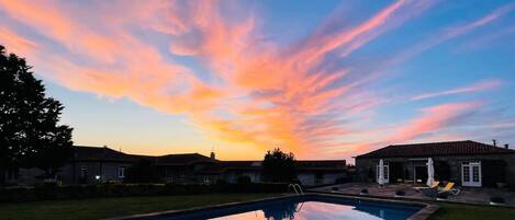 Une piscine offrant une vue dégagée sur le ciel au coucher du soleil, entourée d’un quartier résidentiel avec des maisons et une terrasse.