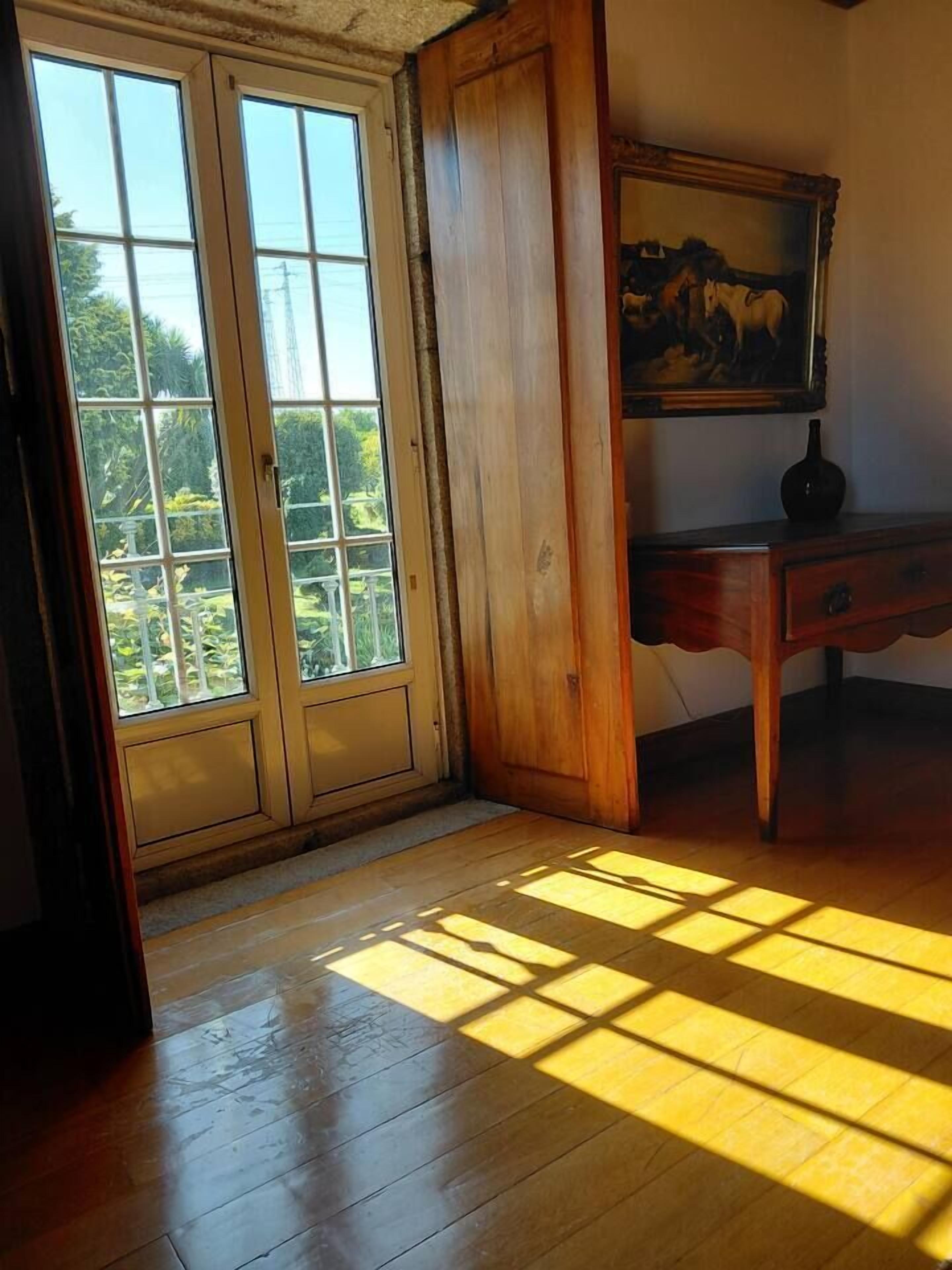 A room with wooden flooring, a door with glass panels, a painting on the wall, and a small table.