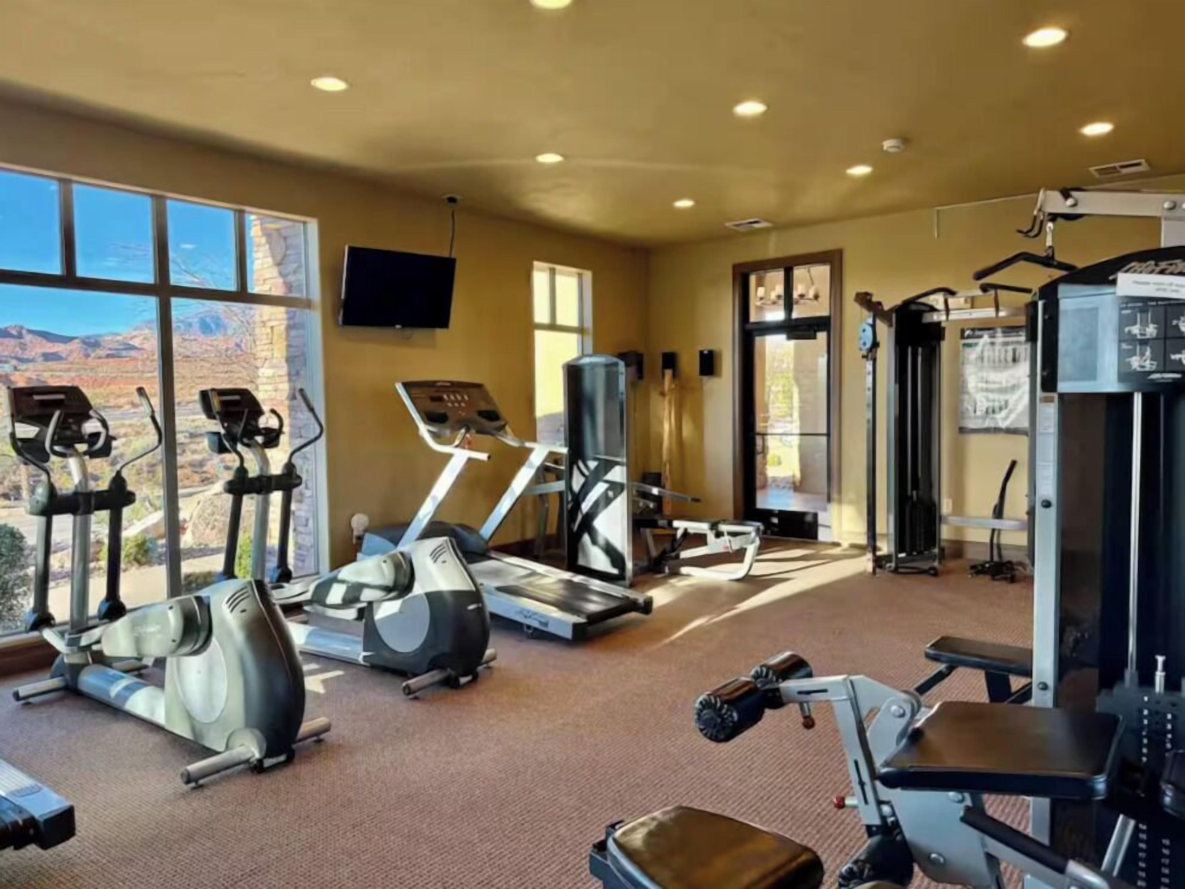 Un gimnasio con máquinas de cardio, equipo de levantamiento de pesas y una pantalla de televisión.