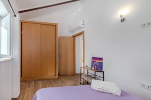A bedroom with a bed, a wooden wardrobe, a painting on the wall, and a bedside table with a lamp. - A Casinha do Limoeiro (Faro)