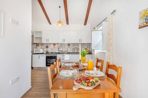 A dining area with a wooden table set for a meal, a kitchen in the background, and a pendant light above. - A Casinha do Limoeiro (Faro)