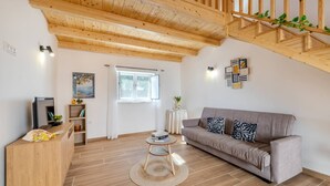 Ein Wohnzimmer mit Holzboden, einem grauen Sofa, einem kleinen runden Tisch und einem Fernseher auf einem Holzboden.