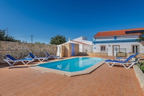 A swimming pool with lounge chairs, a stone wall, and a building with a tiled roof. - A Casinha do Limoeiro (Faro)