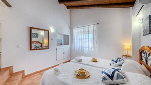 Quarto com cama, espelho, janela com cortinas e uma pequena mesa com abajur.