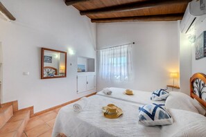 Ein Schlafzimmer mit einem Bett, einem Spiegel, einem Fenster mit Vorhängen und einem kleinen Tisch mit einer Lampe.