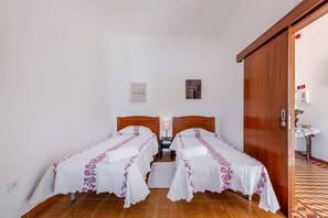 Ein Hotelzimmer mit zwei Einzelbetten, einer Holztür, einem kleinen Tisch mit einem Korb und einer Wandklimaanlage.