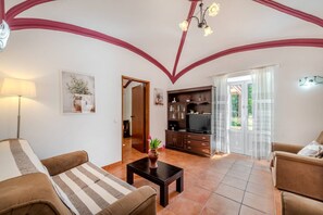 Ein Wohnzimmer mit einer Couch, einem Couchtisch, einer TV-Konsole und einer Tür zu einem anderen Raum.