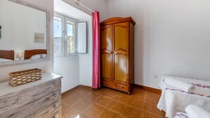 Quarto com guarda-roupa de madeira, espelho, mesa de cabeceira e janela com cortinas.