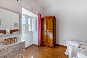 Ein Schlafzimmer mit Holzschrank, Spiegel, Nachttisch und einem Fenster mit Vorhängen.
