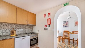 Uma cozinha compacta com máquina de lavar louça, fogão e forno, que dá para uma sala de jantar com mesa e cadeiras.