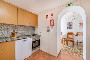 Eine kompakte Küche mit Geschirrspüler, Herd und Backofen, die in einen Essbereich mit Tisch und Stühlen übergeht.