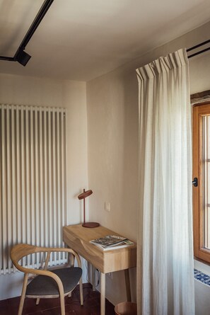 Una habitación con un escritorio de madera, una silla, un radiador y una cortina.