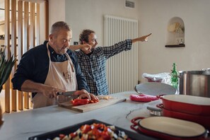 Dos personas en una cocina con tabla de cortar, verduras y utensilios de cocina.