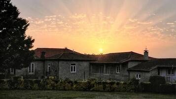 Une maison avec une piscine à l’avant, sous un ciel embrasé par le coucher de soleil.