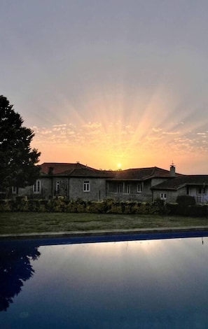A house with a swimming pool in front, under a sunset sky.