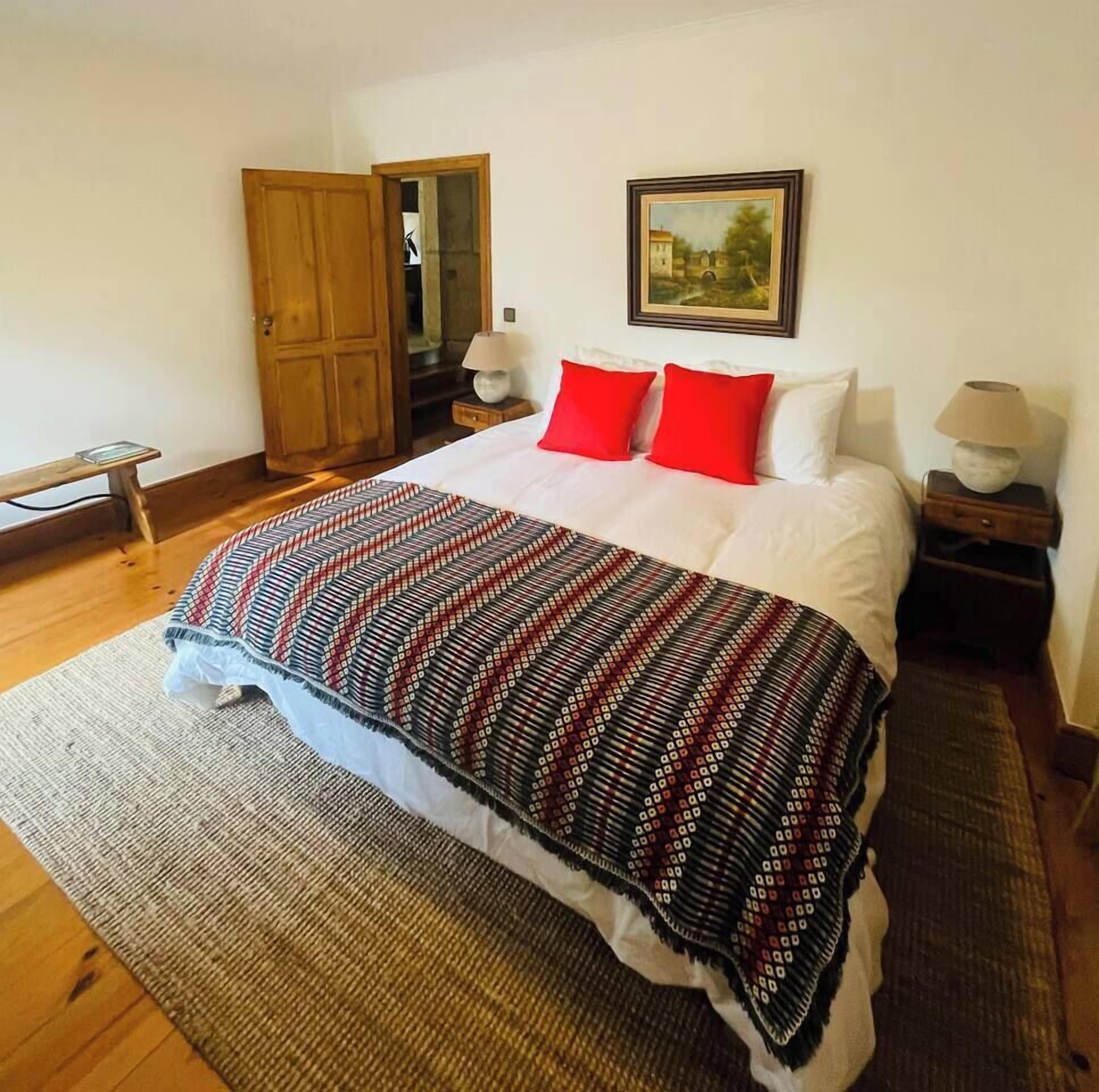 Une chambre à coucher avec un lit, une porte en bois, une table de chevet, une lampe et un tableau au mur.