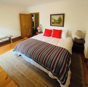 A bedroom with a bed, a wooden door, a nightstand, a lamp, and a painting on the wall.