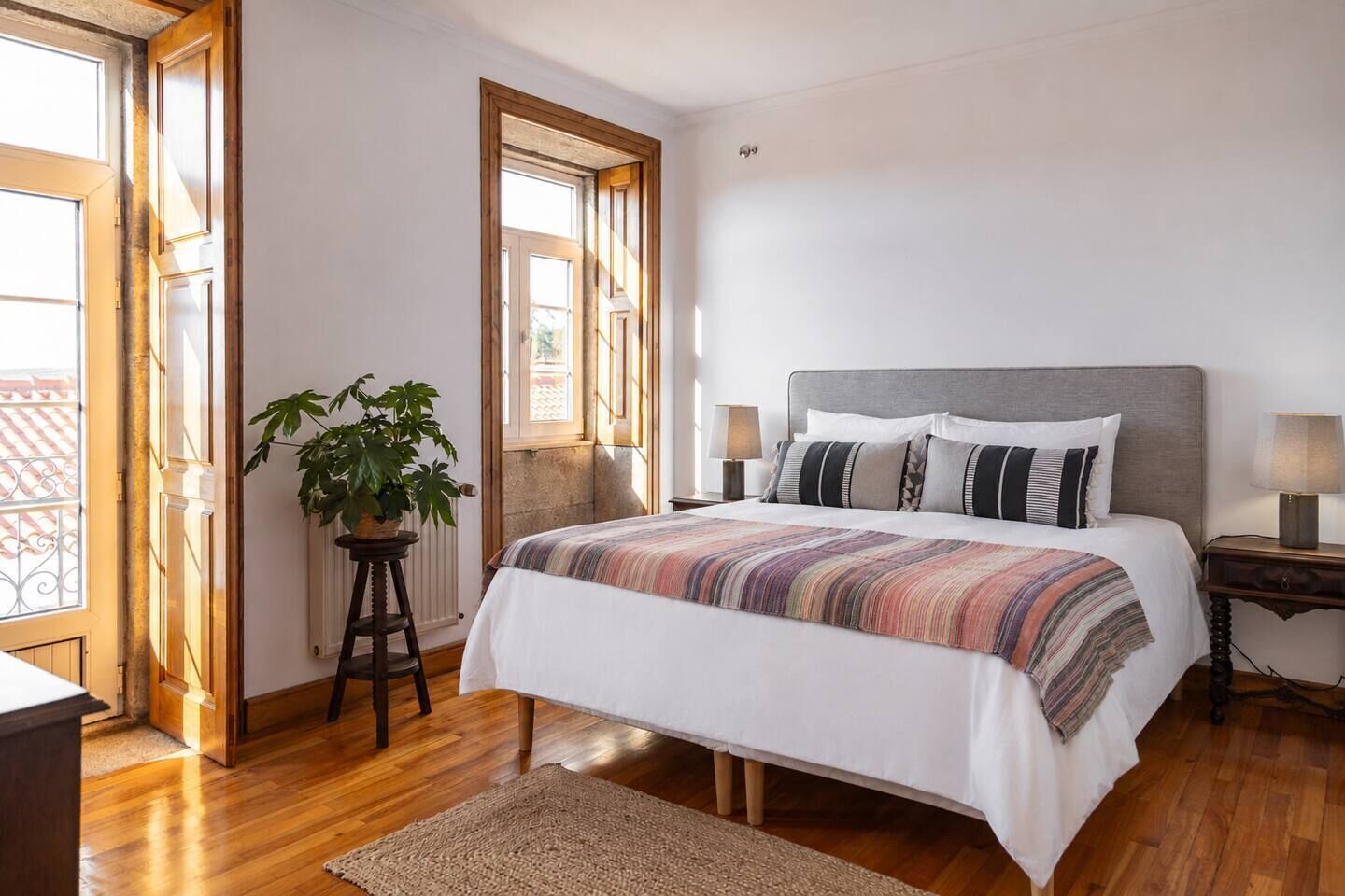 Une chambre avec un grand lit, deux tables de chevet, une plante en pot et une fenêtre.