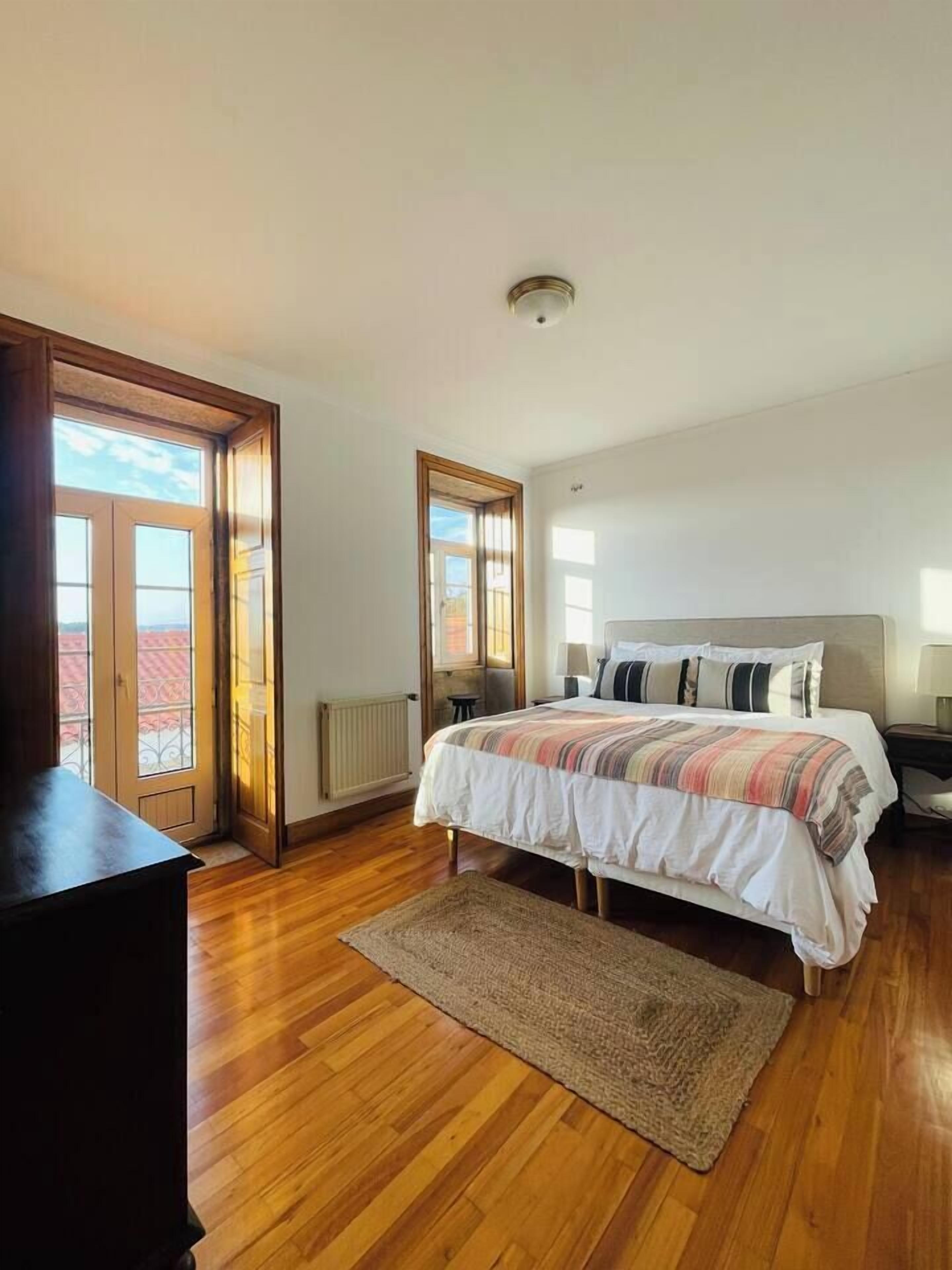A bedroom with a large bed, wooden flooring, a radiator, and a view through a door.