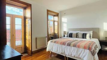 A bedroom with a large bed, wooden flooring, a radiator, and a view through a door.