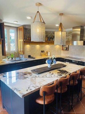 A modern kitchen with a large island, pendant lighting, and a view of the outdoors.