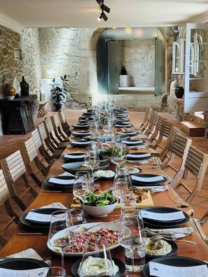A long dining table set for a meal with multiple chairs, a stone wall in the background, and a stone fireplace. - Quinta Esmeralda - Private Estate (Mosteiró)