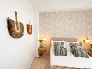 Un dormitorio con una cama, dos mesitas de noche, lámparas de pared y un papel tapiz con motivos florales.