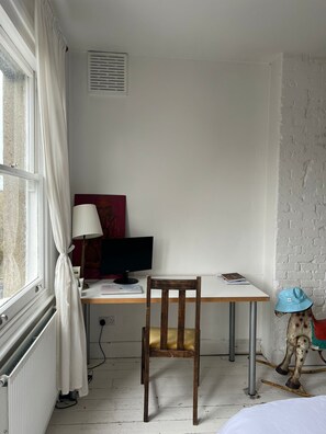A room with a wooden desk, a computer, a lamp, a radiator, and a window with curtains. - Bright, Calm and Trendy 2 Bedroom West London Flat (London)