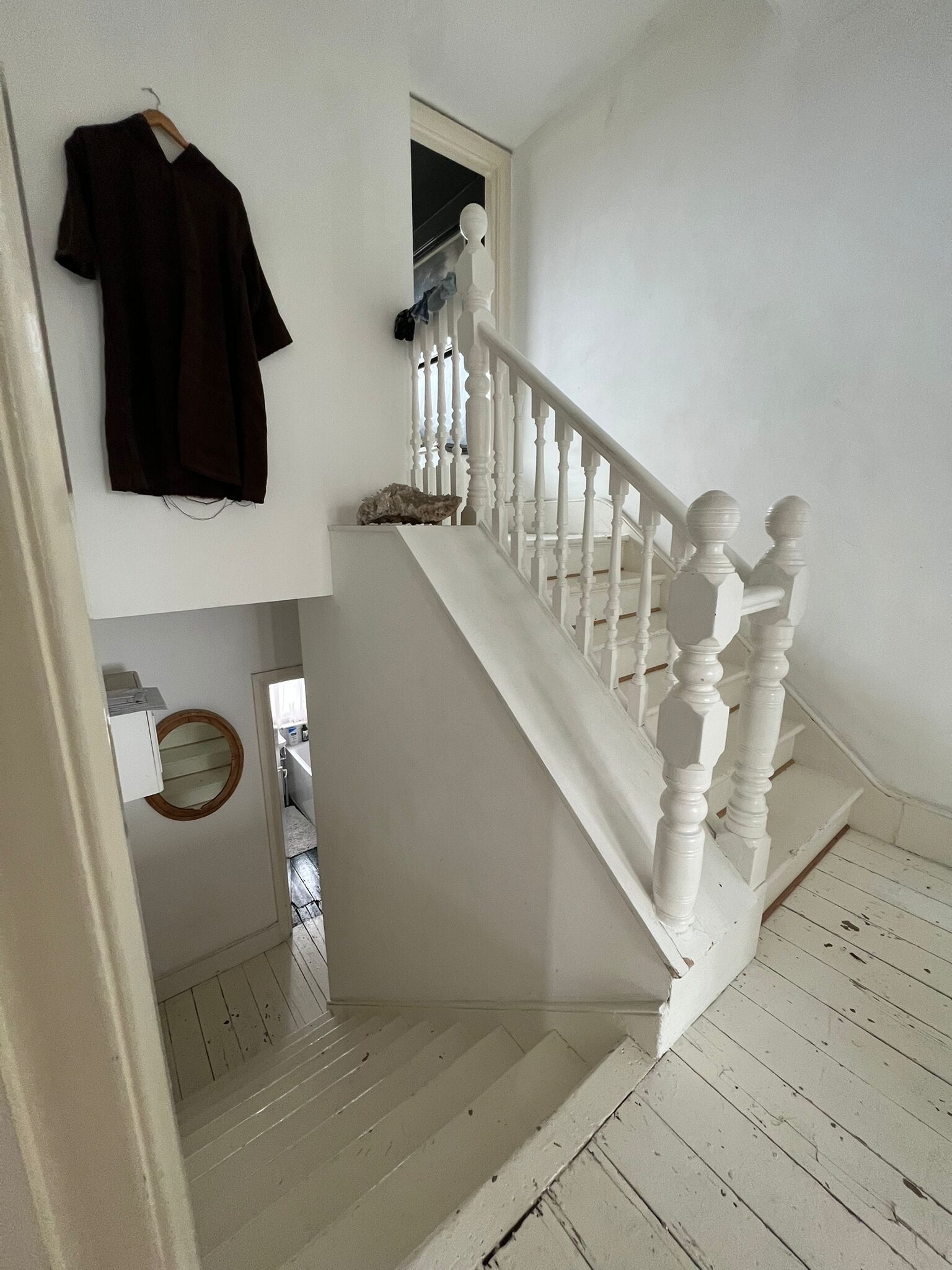 A white wooden staircase with a white balustrade, leading to a landing with a mirror and a hanging garment.