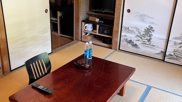 A traditional Japanese room with tatami flooring, a wooden table, a television, and a sliding door. - ARASAWAYA RYOKAN (Okutama)