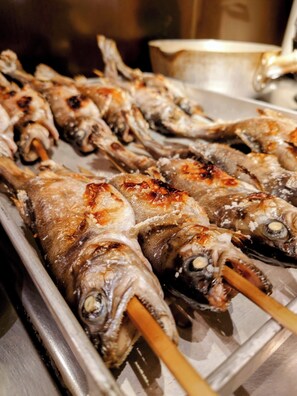Pescado a la parrilla ensartado en brochetas dispuesto en una bandeja.