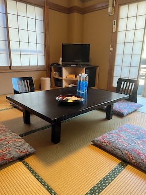 Una habitación con tatami, una mesa baja, sillas, un televisor y un refrigerador pequeño.