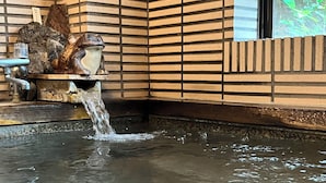 A hot spring with water flowing over a wooden edge, surrounded by a tiled wall with a brick pattern. - ARASAWAYA RYOKAN (Okutama)