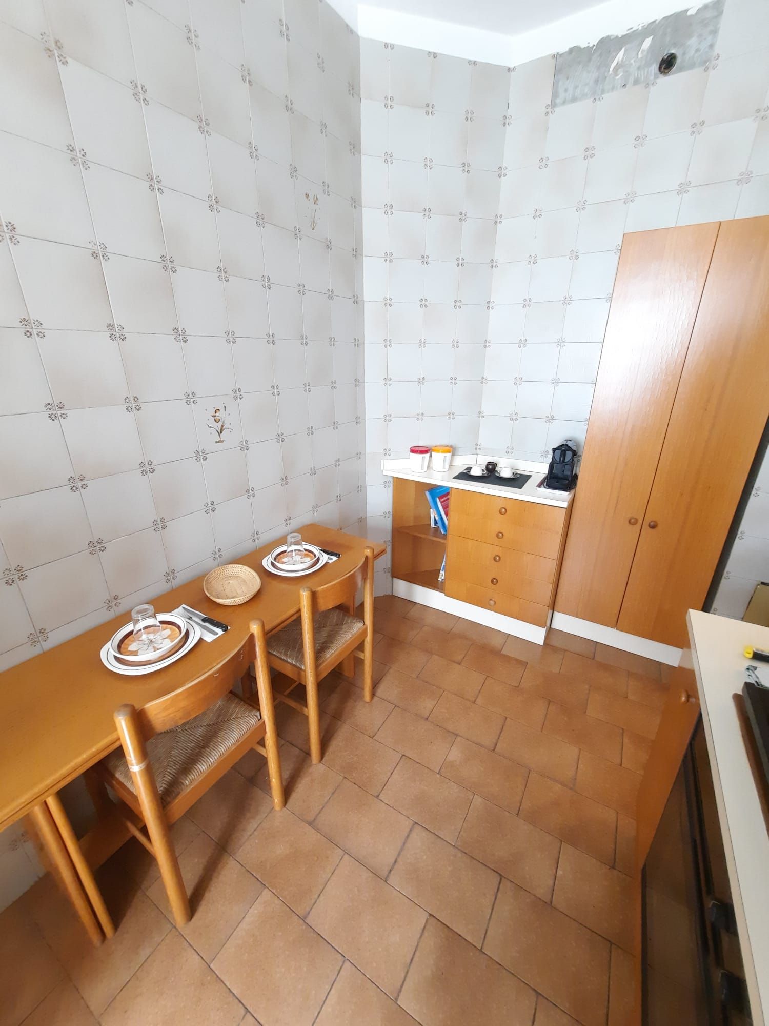 A compact kitchen with a wooden table, chairs, and a small countertop with a kettle and cups.