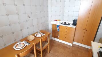 A compact kitchen with a wooden table, chairs, and a small countertop with a kettle and cups.