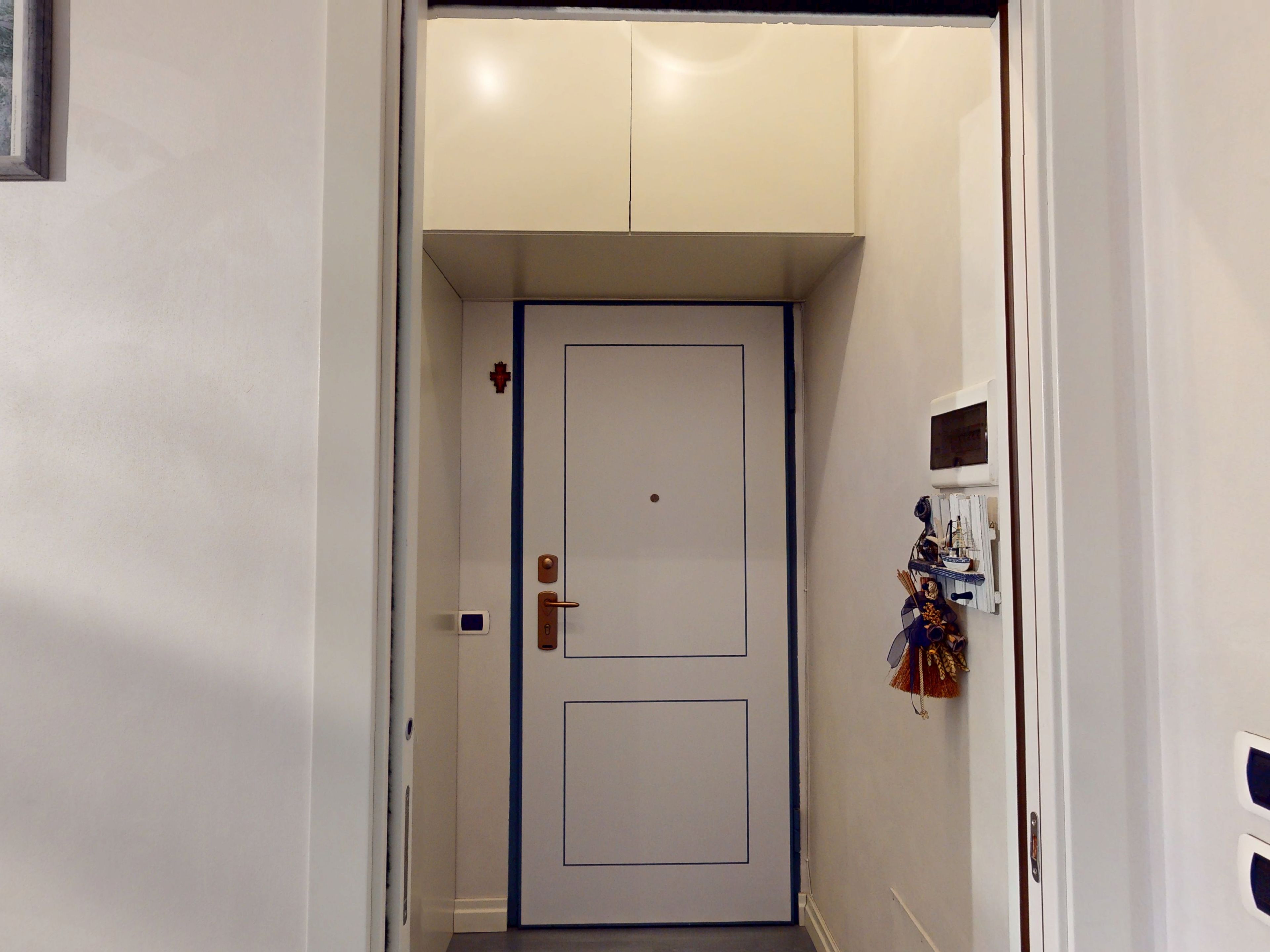 Ein schmaler Flur mit einer geschlossenen Tür, einer kleinen Wanddekoration und einem Thermostat an der Wand.