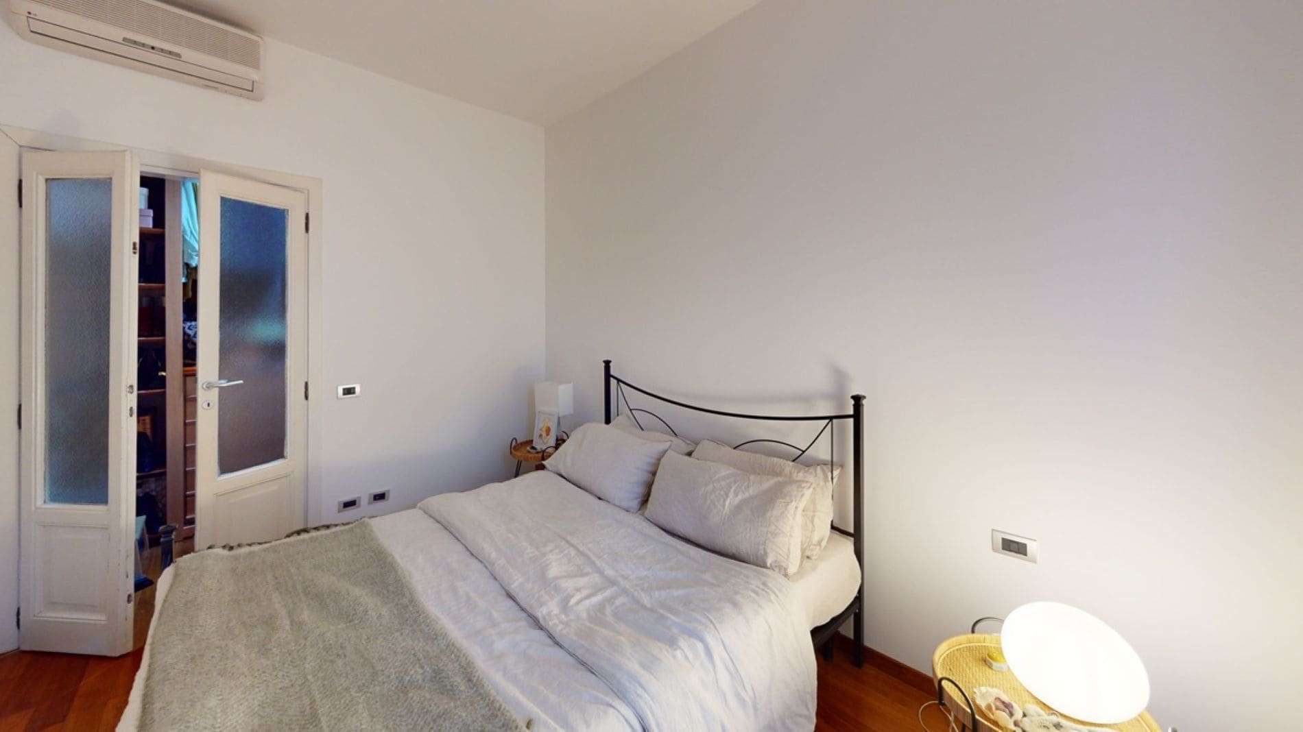 Ein Schlafzimmer mit Bett, Nachttisch, Lampe, Kleiderschrank und Spiegel.