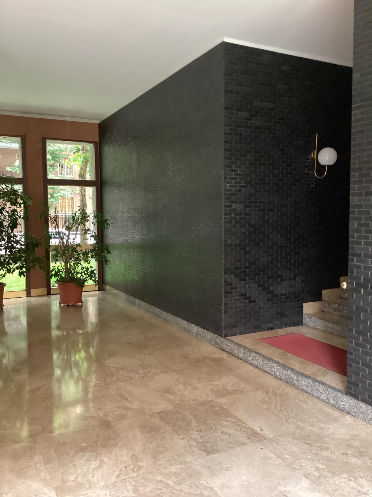 A lobby with a polished floor, a dark textured wall, and a staircase with a red carpet.