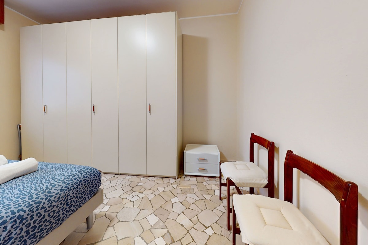 A bedroom with a bed, a wardrobe, a small bedside table, and two chairs.