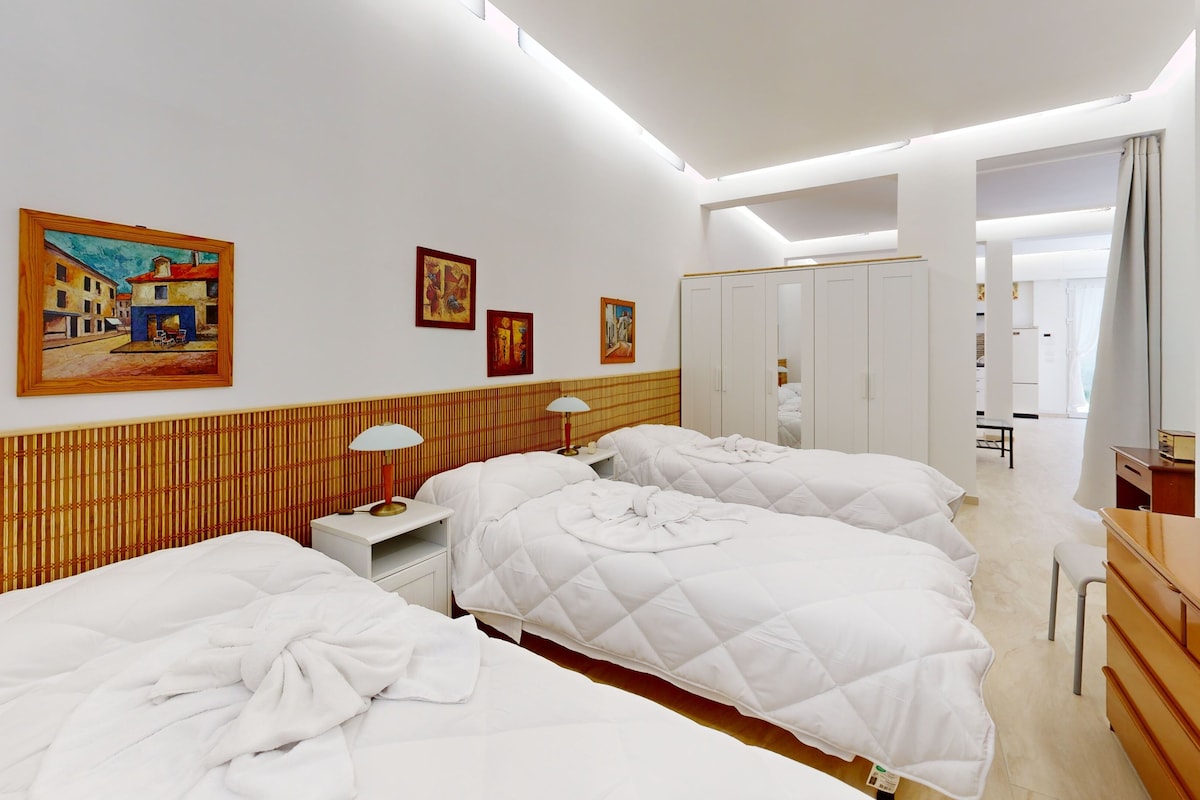 A hotel room with two beds, a bedside table with a lamp, a wardrobe, and a painting on the wall.